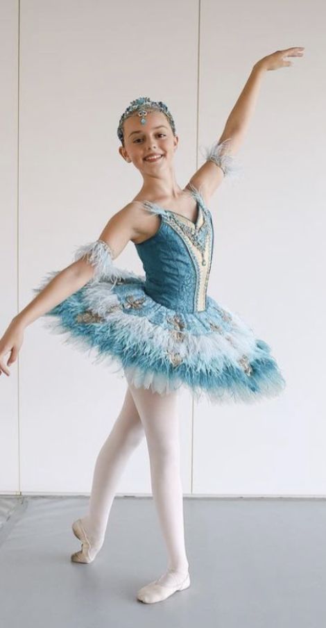 a young ballerina in a blue tutu and feathered skirt is posing for the camera