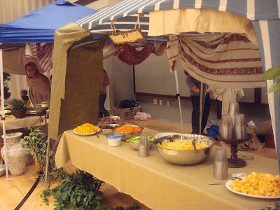 a tent set up with food on the table and people standing around eating from bowls