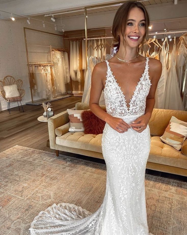 a woman standing in front of a couch wearing a white wedding dress with lace detailing