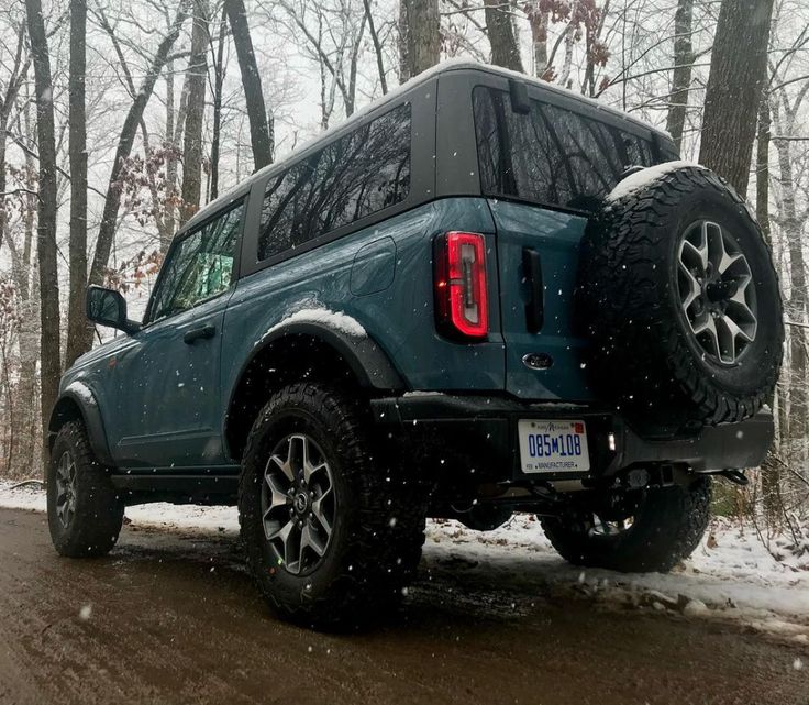 a blue truck parked on the side of a road in front of snow covered trees