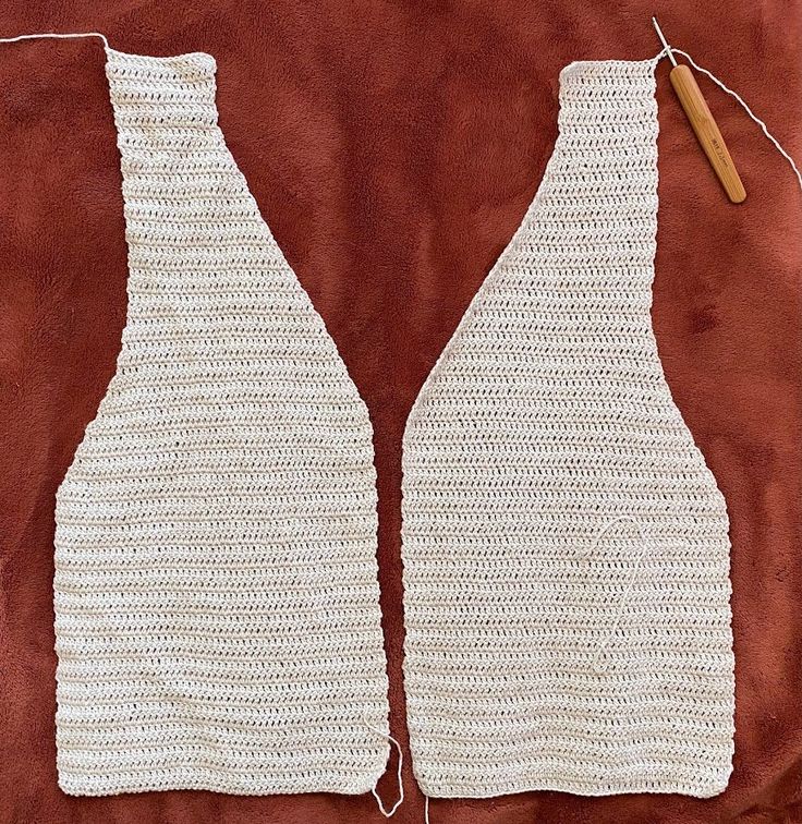 two crocheted vests are next to a knitting needle on a red cloth