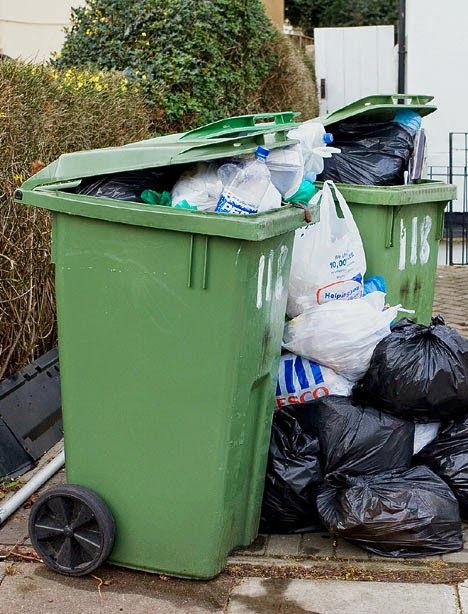 a pile of garbage sitting on top of a sidewalk next to a green trash can