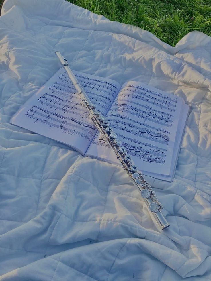 an open book and flute laying on a blanket in the grass with sheet music notes