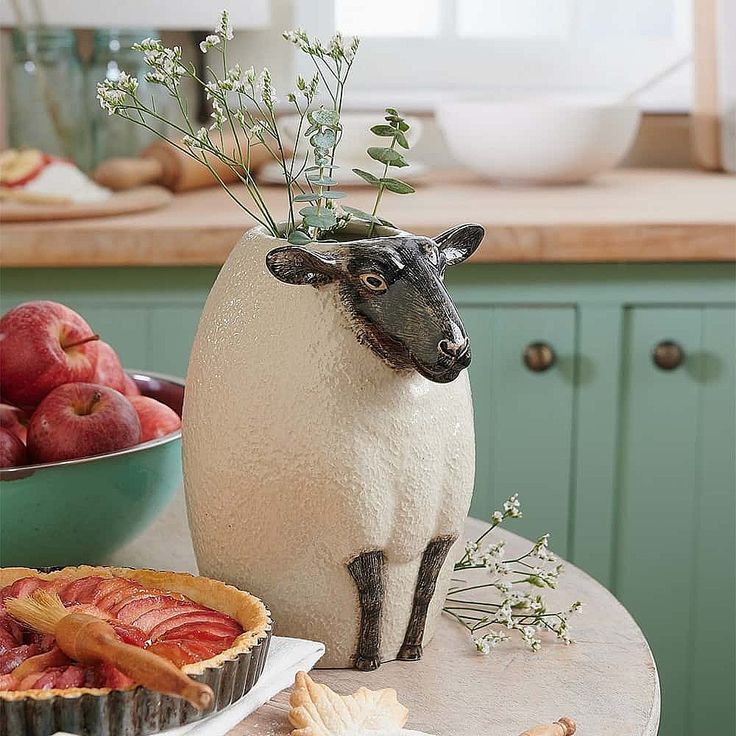 a sheep figurine sitting on top of a table next to pies and fruit