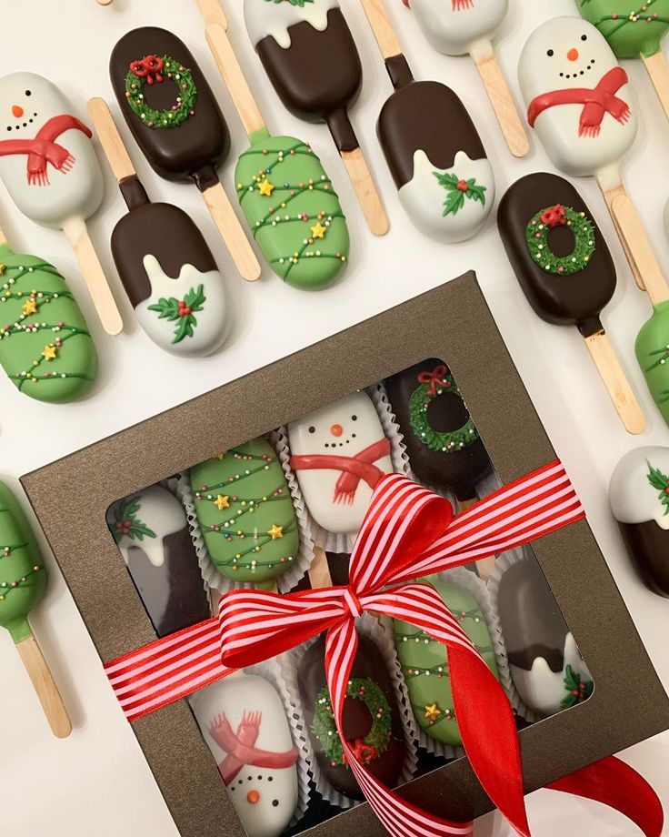 a box filled with green frosted christmas cookies next to chocolate covered marshmallows