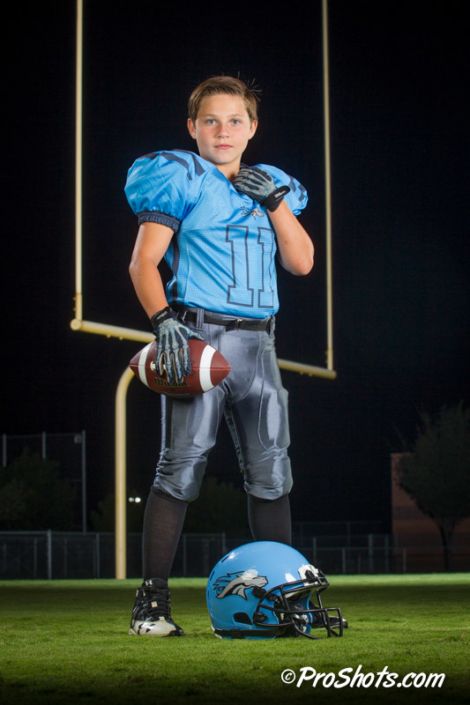 a football player is posing with his helmet and ball on the sidelines at night