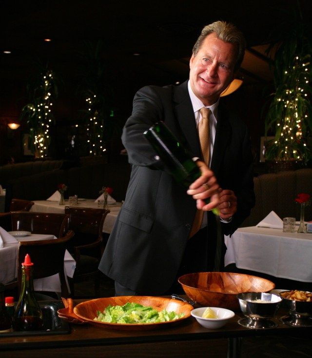 a man in a suit and tie holding a wine bottle next to a table with food on it