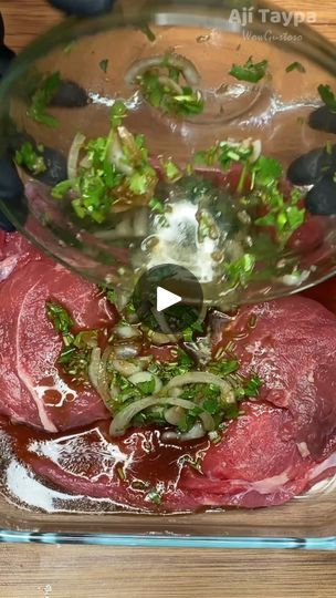 raw meat being prepared in a glass bowl with herbs and seasonings on the side