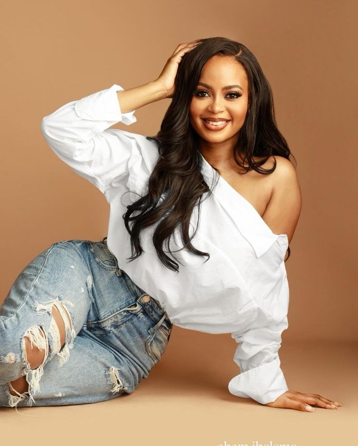 a woman sitting on the ground wearing ripped jeans and a white shirt with long sleeves