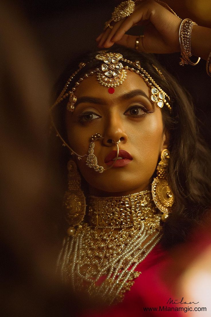 a woman with gold jewelry on her face and hands behind her head, looking into the distance