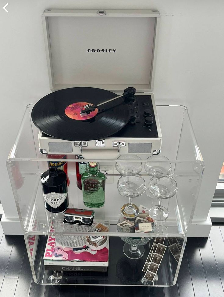 a record player and some wine glasses on a clear shelf in front of a window