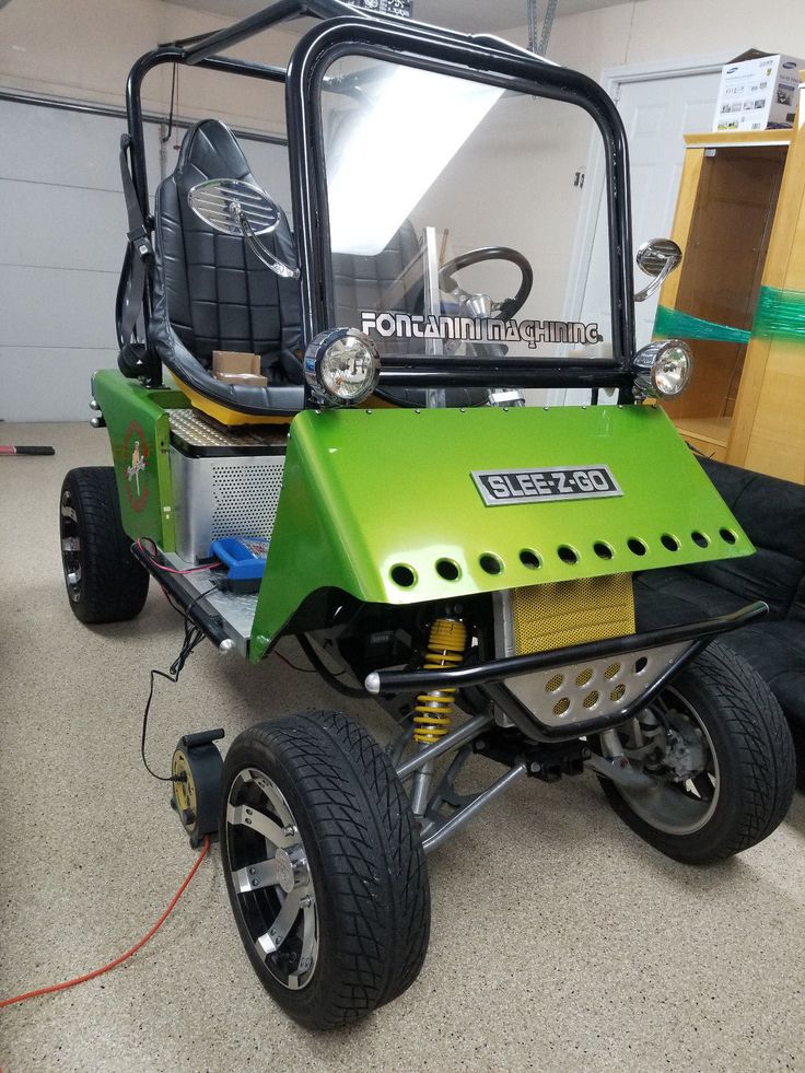 a small green vehicle parked in a garage next to a black bag on the floor