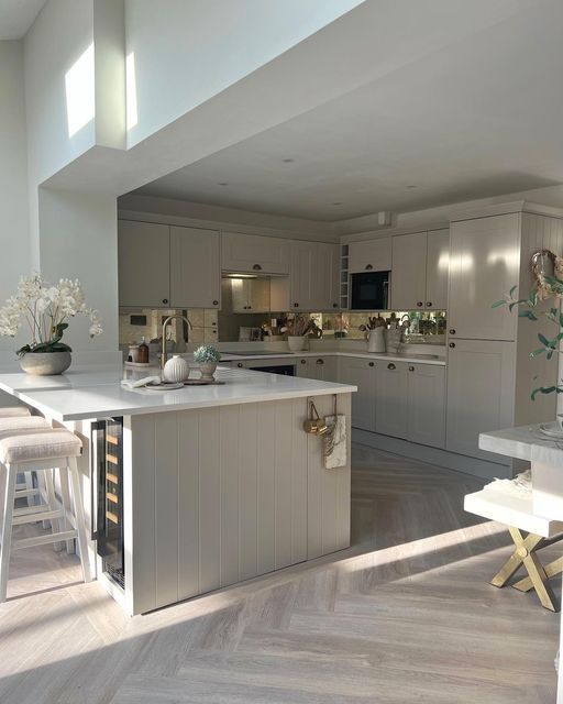 a large kitchen with white cabinets and wooden flooring in the middle of an open living room