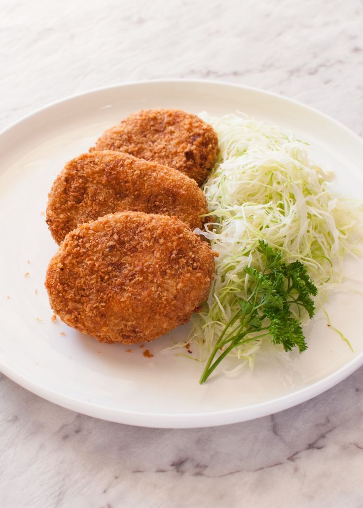 two fried meat patties on a white plate with shredded cabbage and garnish