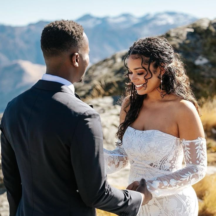 a man and woman standing next to each other in front of some mountains with snow on them