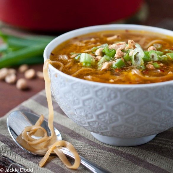 a white bowl filled with soup next to a spoon and green beans on a table