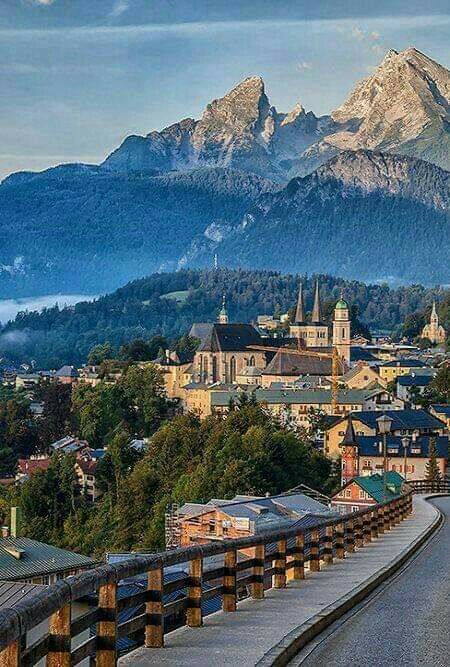 a scenic view of a town with mountains in the background and a bridge leading to it