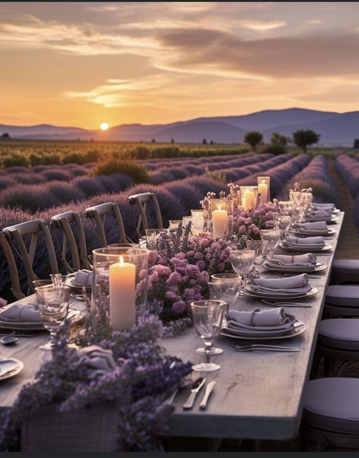 a long table is set with candles and plates in front of lavender fields at sunset