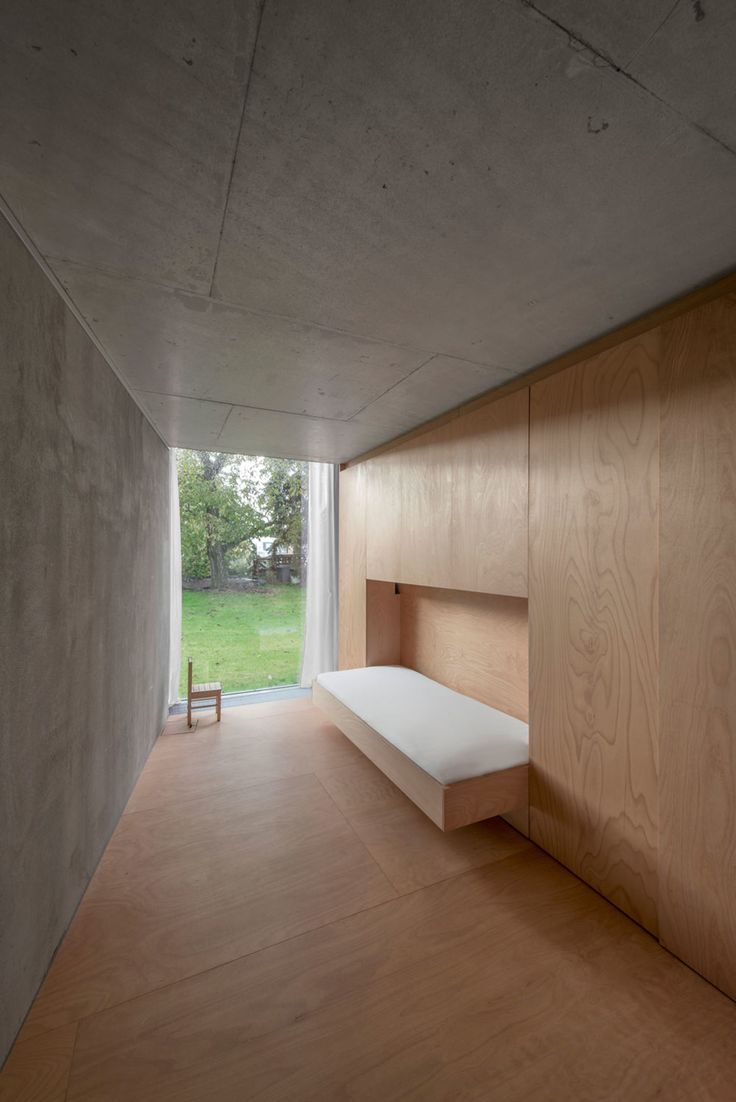 an empty room with wood paneling and white bed in the center, looking out onto a grassy field