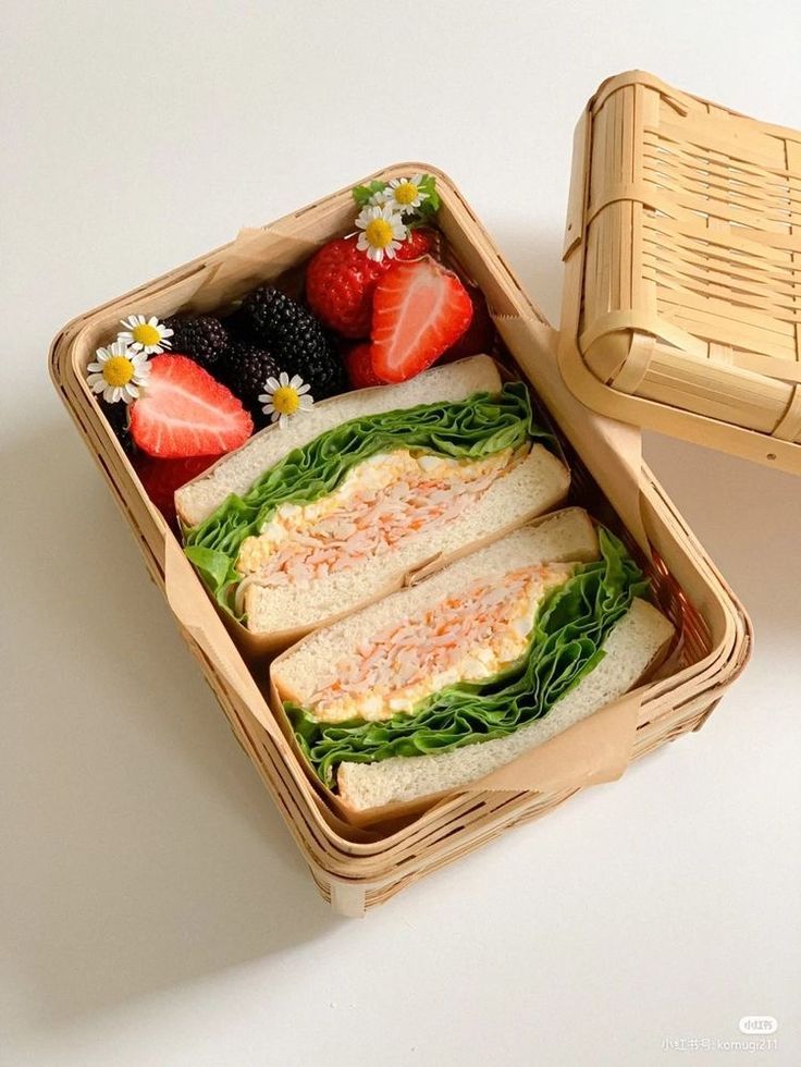 an open lunch box with sandwiches and strawberries on the side, next to a wicker basket