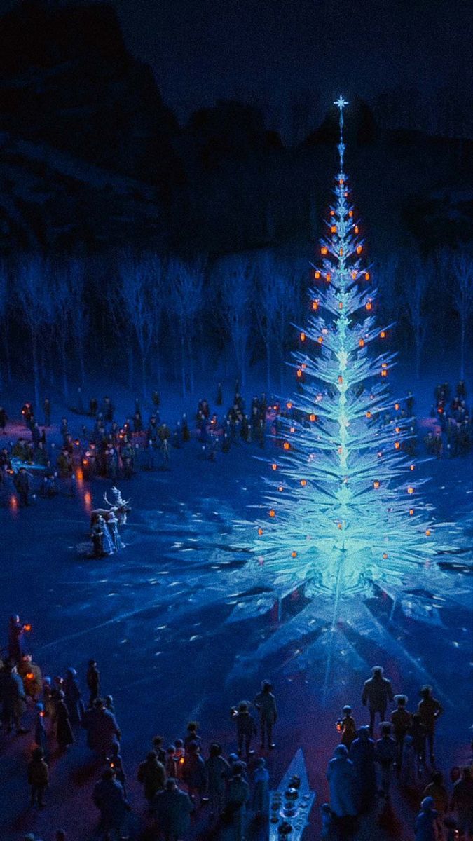 a group of people standing around a lit up christmas tree in the middle of a snow covered field