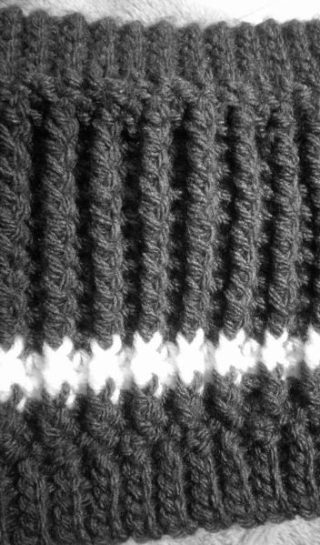 a black and white photo of a crocheted scarf on a bed with a pillow behind it