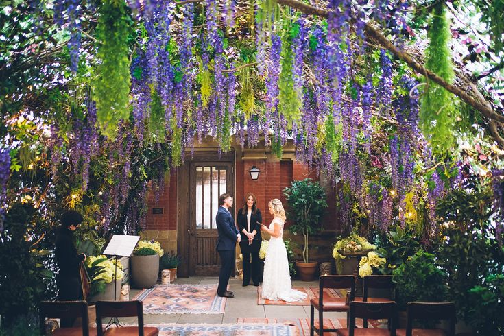 a bride and groom standing in front of an archway with purple flowers hanging from it