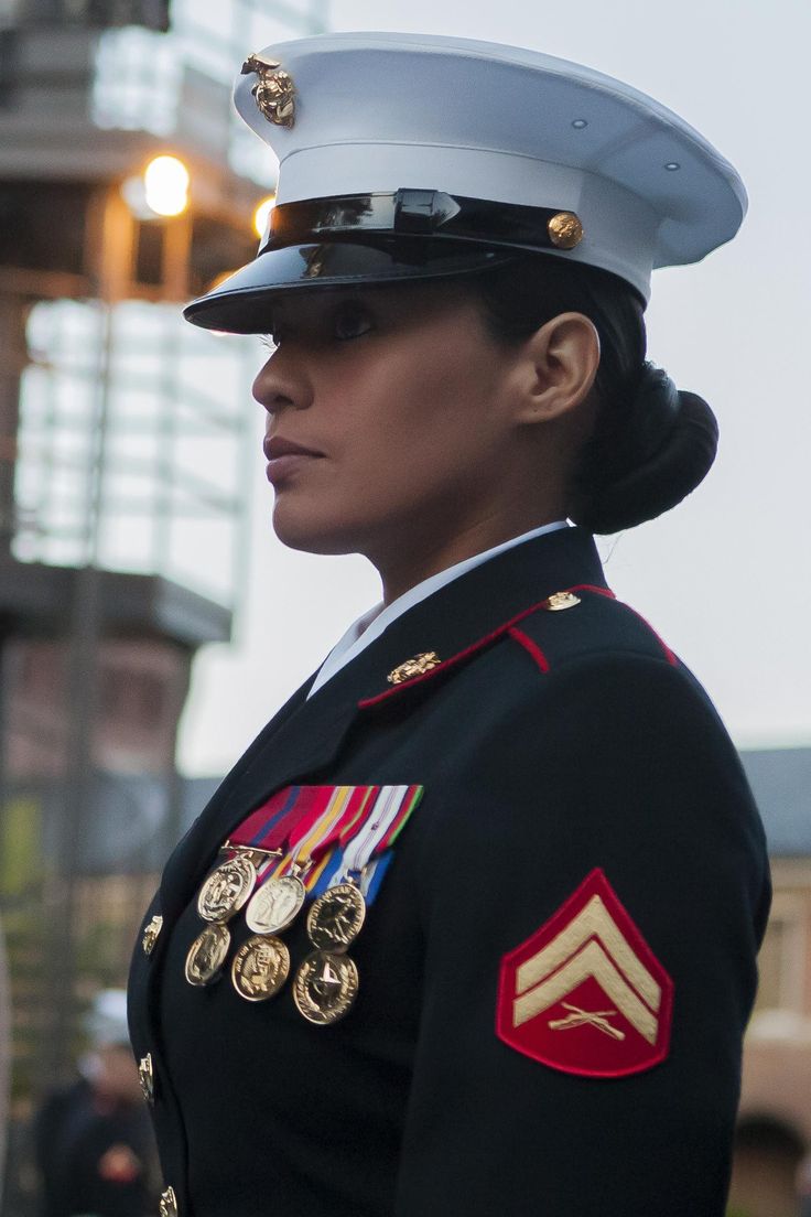 a woman in uniform is standing on the street with other people behind her and looking off into the distance