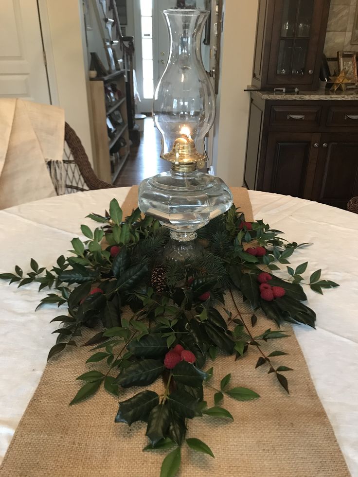 a candle is lit on top of a table covered with greenery and berries in a vase