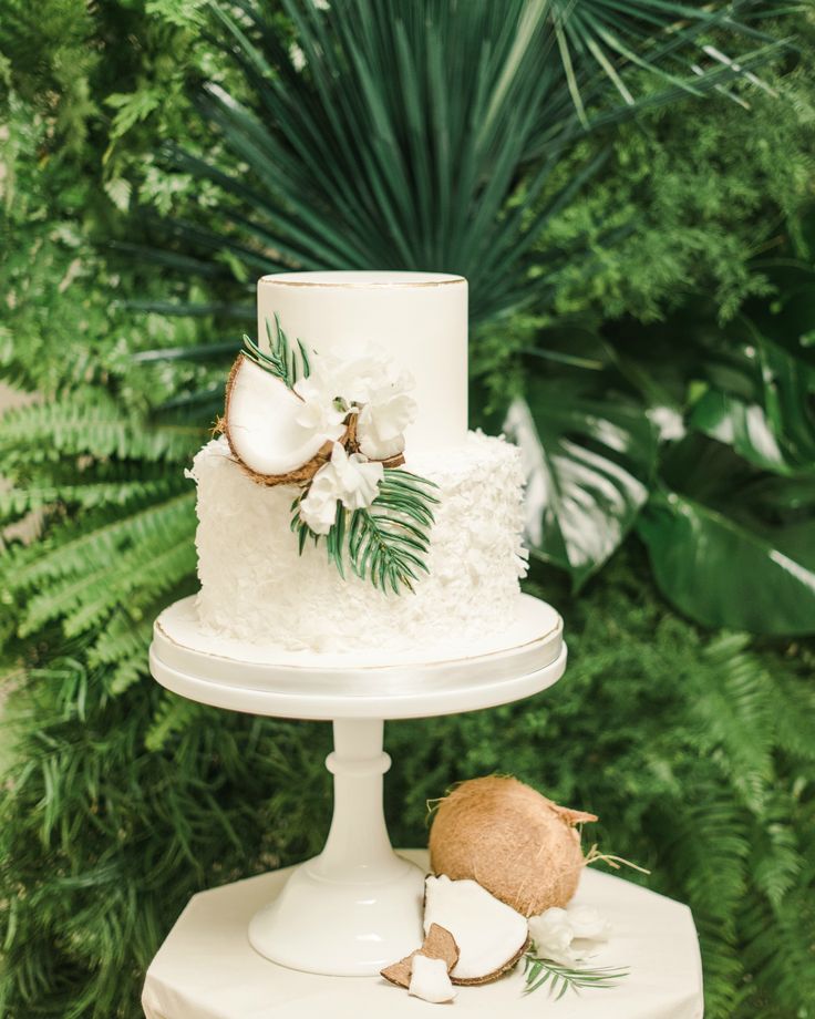 a three tiered cake with coconuts and flowers on top is sitting on a white pedestal