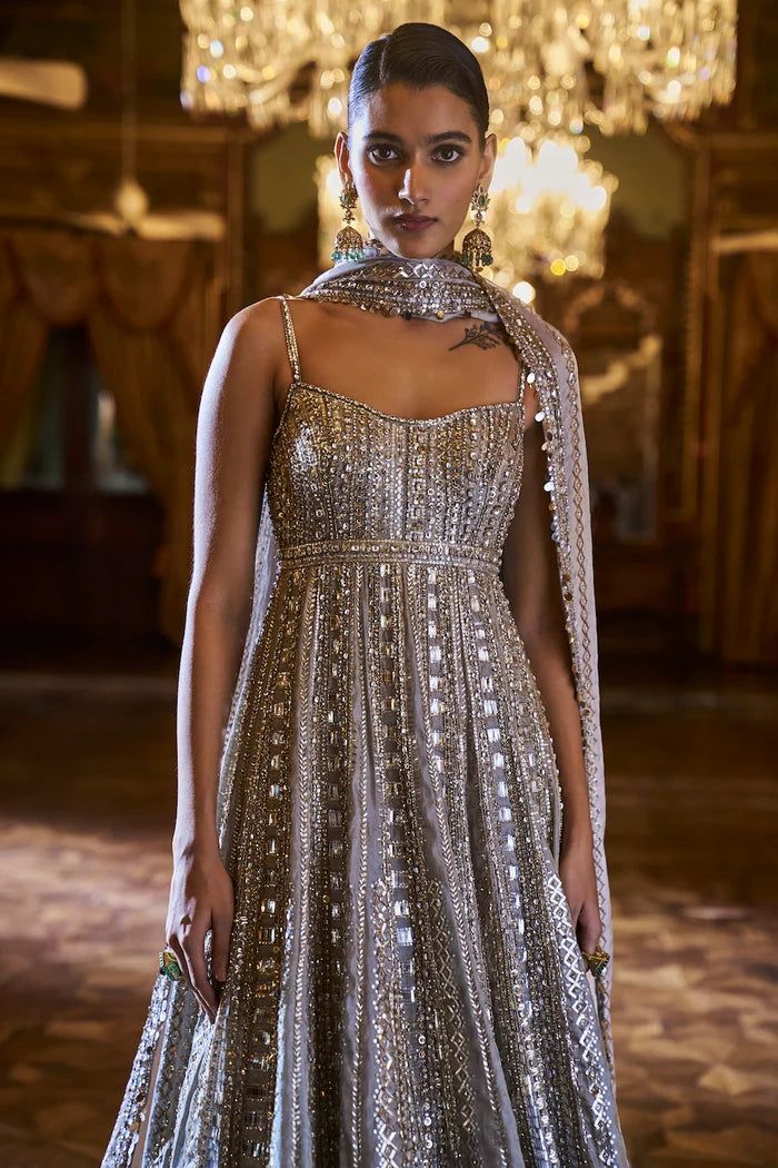 This sharara set features sequin and mirror embroidery in tones of gold and silver in a linear pattern. The contrasting nude tissue silk sharara has a broad border at the hem. It is paired with an embroidered silver tissue silk dupatta.From Seema Gujral's Falaknuma collection. DELIVERY TIMEPlease allow 8-12 weeks for your outfit to arrive. FABRIC DETAILSTissue Silk Professional cleaning only. Luxury Gold Art Silk Sharara, Silver Designer Wear Sharara For Eid, Designer Silver Sharara For Eid, Silver Sharara With Zari Work For Eid, Silver Sharara For Designer Wear And Eid, Silver Anarkali Set For Festive Designer Wear, Festive Anarkali Style Silver Sharara, Anarkali Silver Salwar Kameez With Mirror Work, Festive Silver Salwar Kameez With Mirror Work