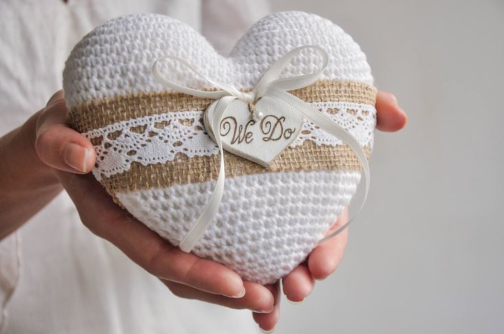 a person holding a crocheted heart shaped box with a monogram on it