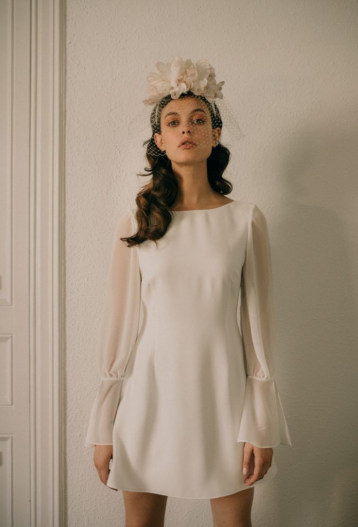 a woman in a short white dress with flowers on her head standing against a wall