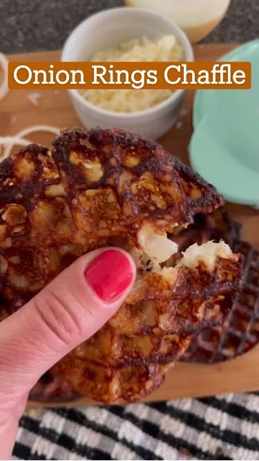 a person holding up a piece of food on top of a wooden cutting board with the words onion rings chaffle