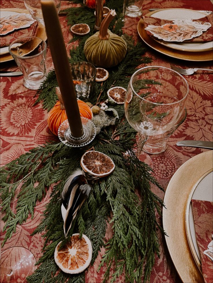 the table is set for thanksgiving dinner with oranges and greenery on top of it