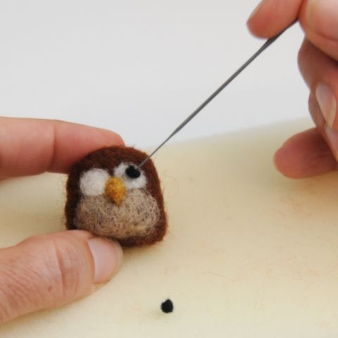 someone is needleing something in to a small stuffed animal that looks like an owl