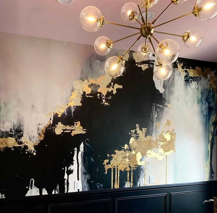 a chandelier hanging from the ceiling in front of a wall with black and gold paint