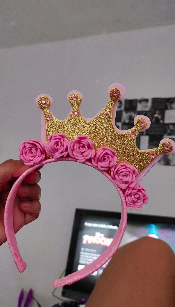 a person is holding a pink and gold tiara with roses on it in front of a tv