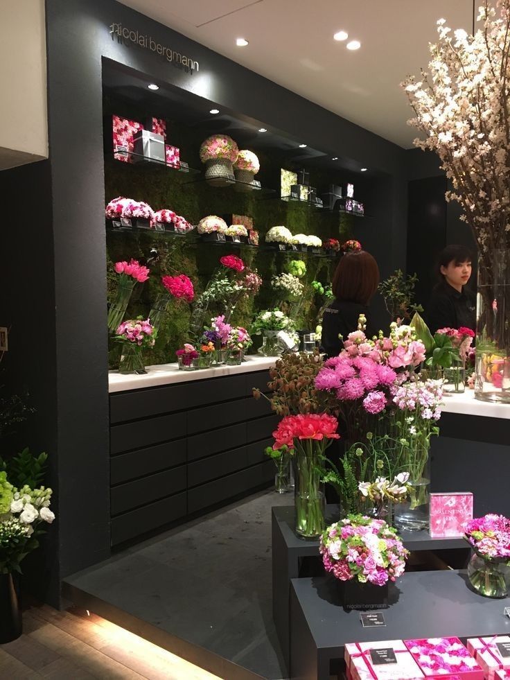 a flower shop with flowers in vases and people looking at the floral arrangements on display