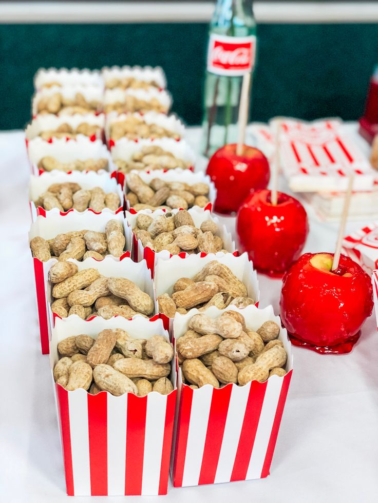 there are many red and white striped bags with nuts in them on the table next to apples