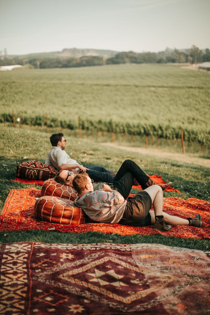 two people sitting on a rug in the middle of a field with an orange blanket