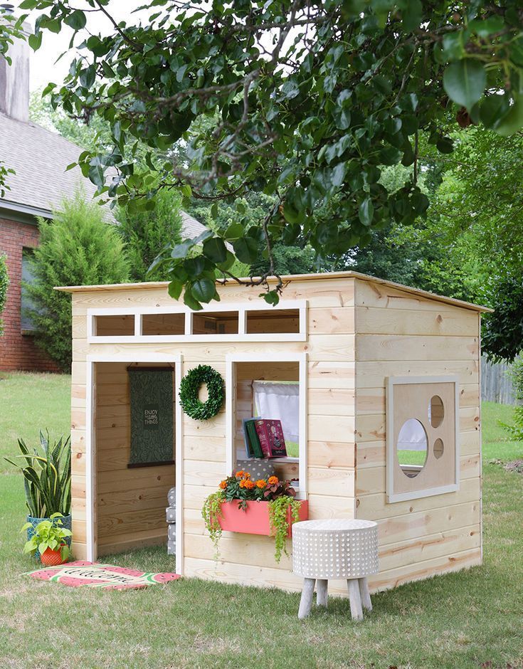 a small wooden shed sitting on top of a lush green field next to a tree