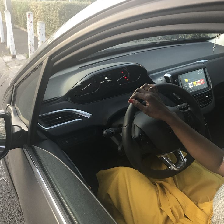 a woman driving a car on the road with her hand on the steering wheel and wearing yellow pants