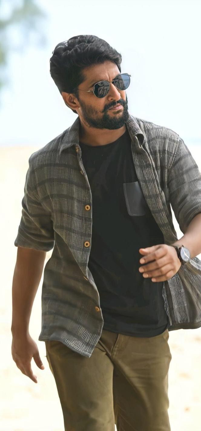 a man with sunglasses and a black shirt is standing on the beach looking at something