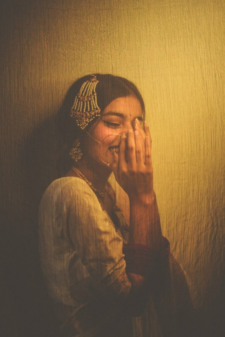 a woman is smiling and covering her face with her hands while standing in front of a wall