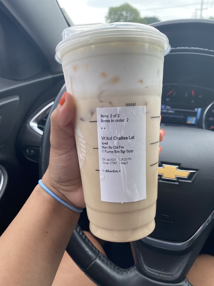 a woman holding up a cup of coffee in her car with the label on it