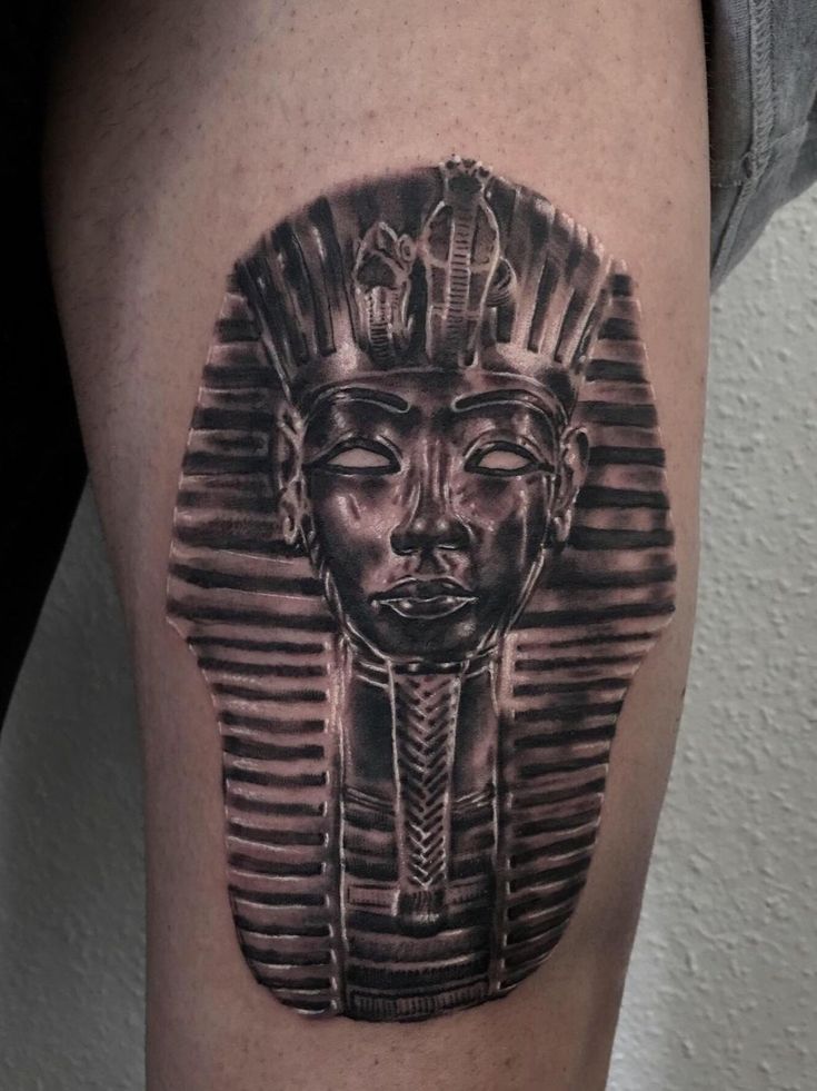 a black and white photo of an egyptian mask on the thigh, done by tattoo artist steve