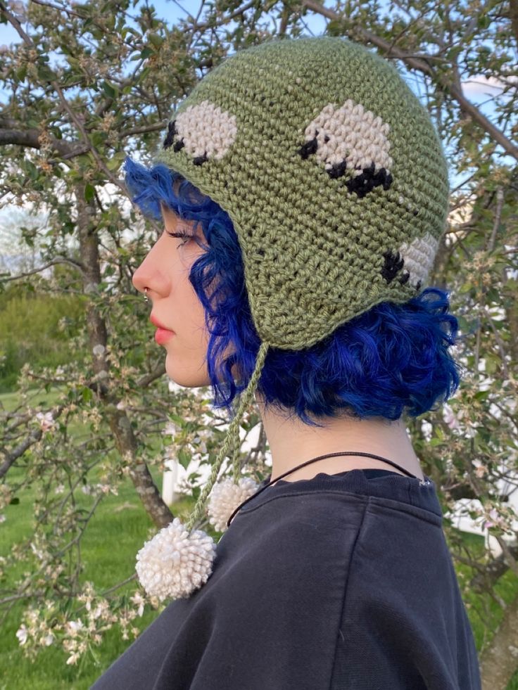 a woman with blue hair wearing a green crocheted hat in front of a tree