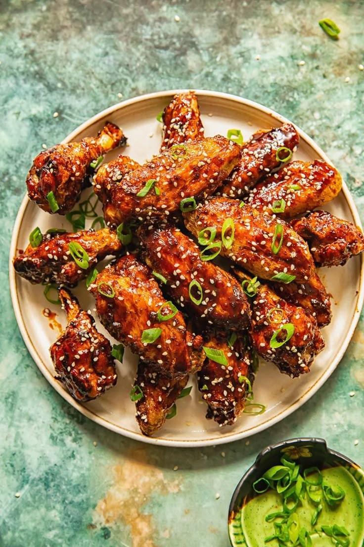 chicken wings covered in sesame seeds and green onions on a plate next to dipping sauce