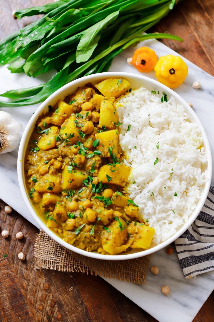 a white bowl filled with rice and curry next to green onions on a wooden table